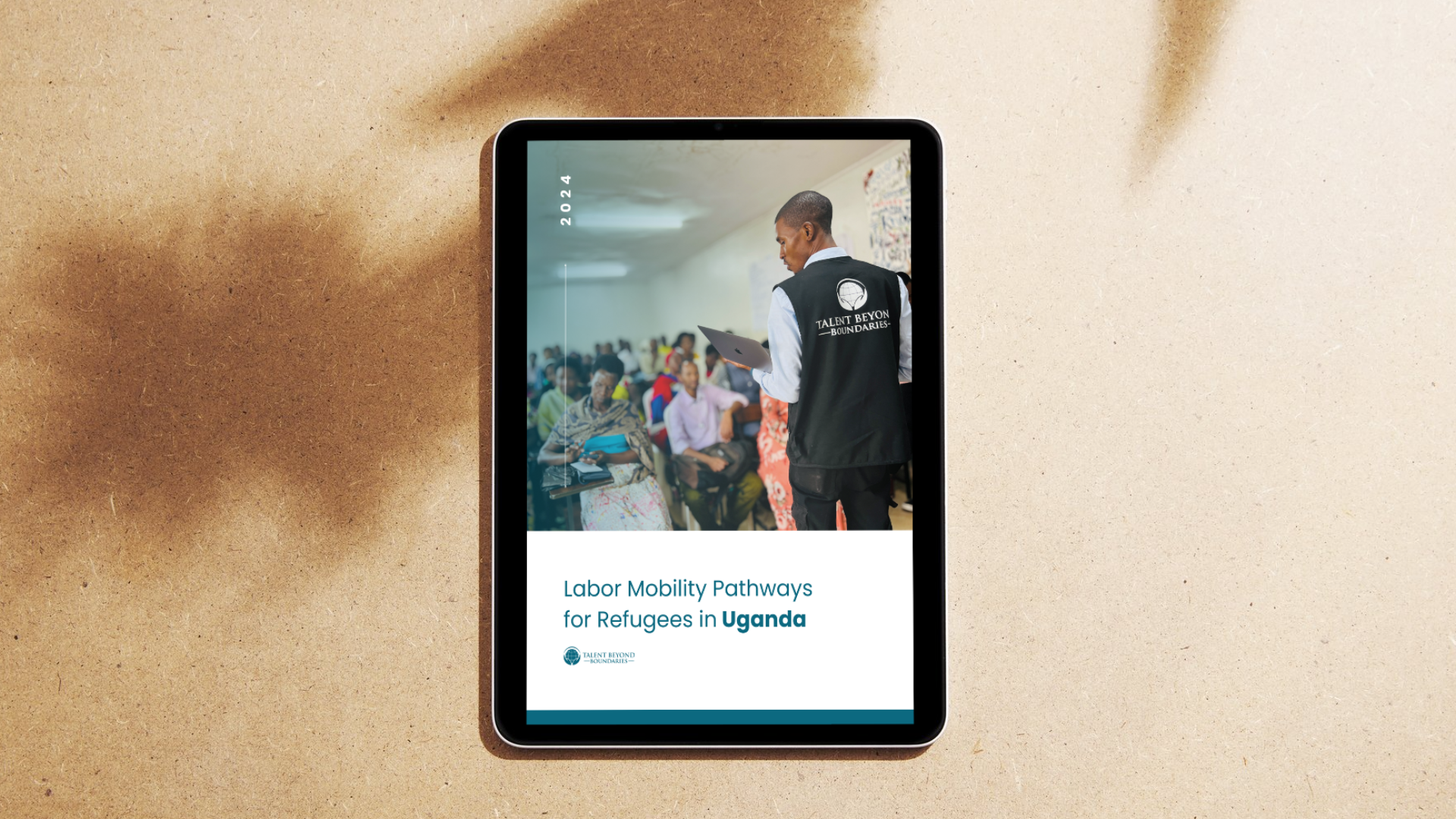 Tablet displaying a report titled "Labor Mobility Pathways for Refugees in Uganda" with a photo of a man in a black vest and white shirt presenting to an audience.