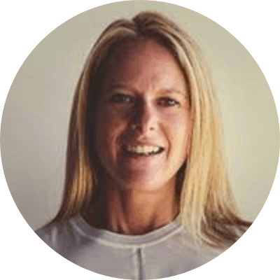 A woman with long blonde hair and light skin, smiling at the camera, wearing a white top.